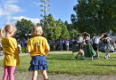 Kinder tanzen in Trachten auf einer Wiese neben dem Maibaum.